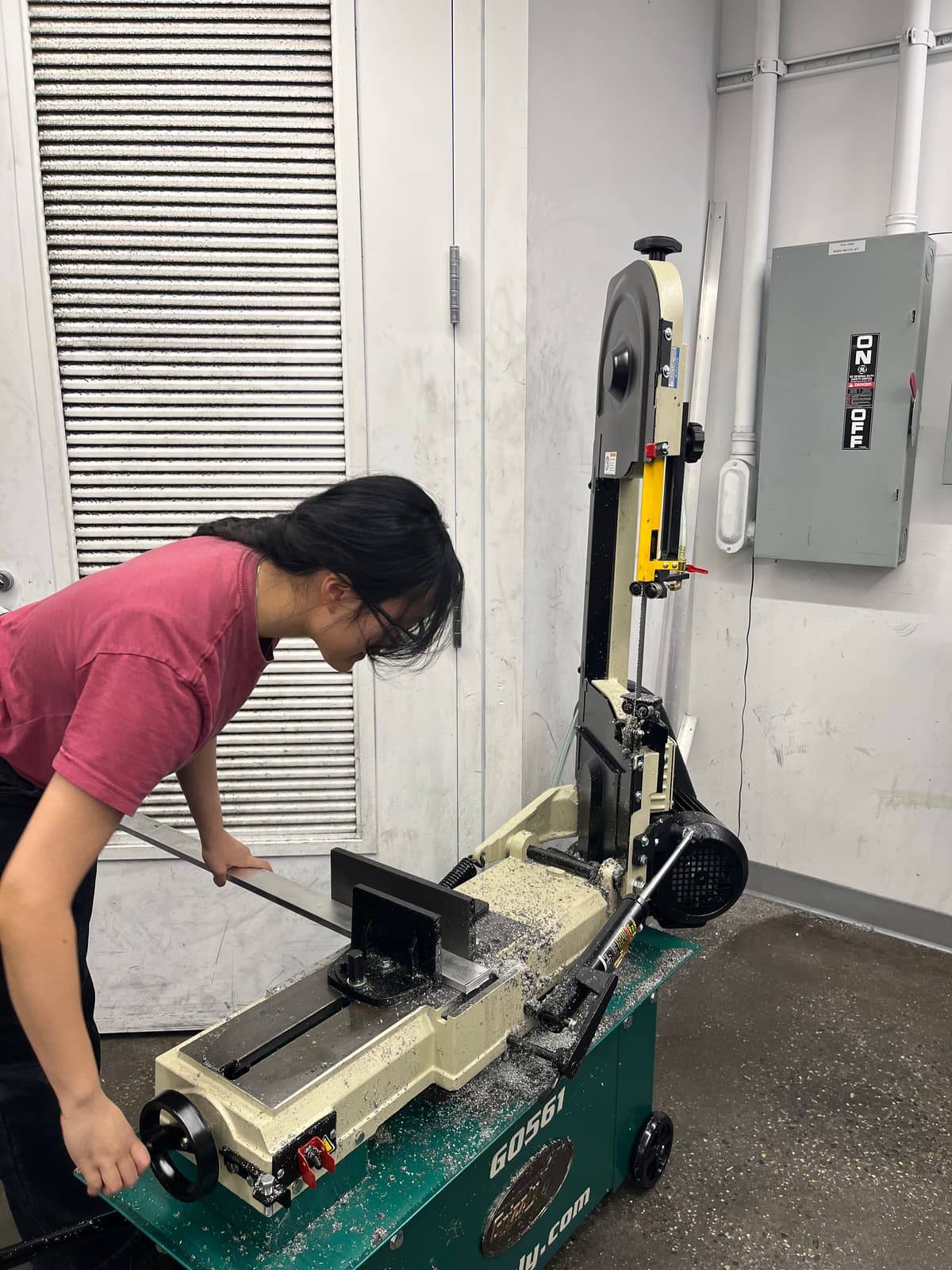A team member cutting metal stock on a horizontal bandsaw in the machine shop.