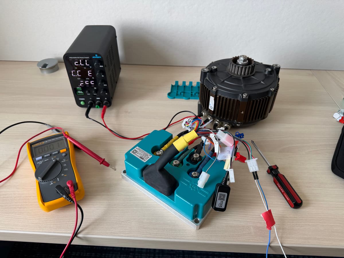 A traction motor, motor controller, and multimeter set up on a bench for controller commissioning.