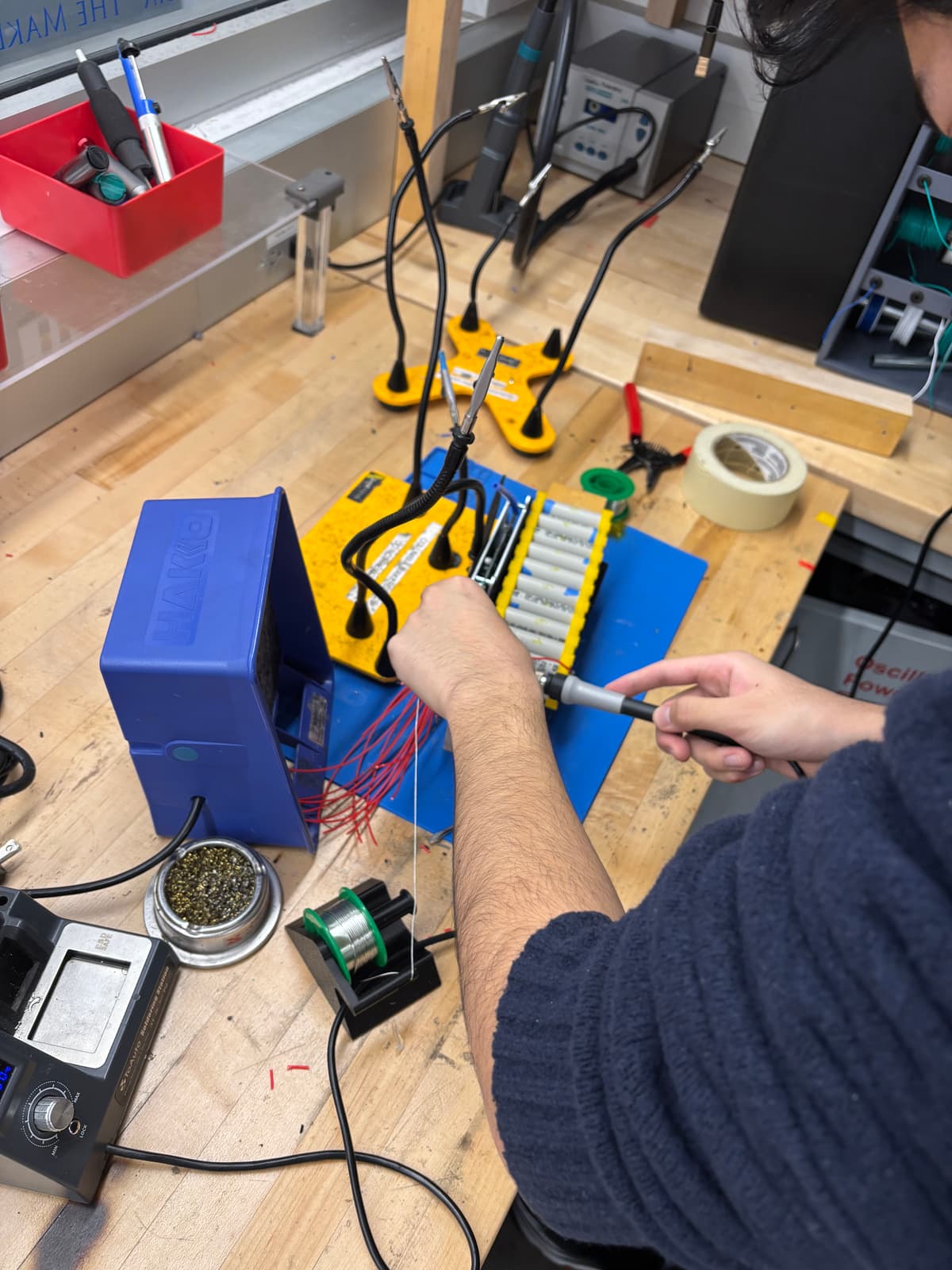 A team member soldering balance leads onto a battery module at an electronics bench.